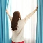A woman with long brown hair stands by a window, emphasizing light in a home, highlighting B & D Plumbing's HVAC services.