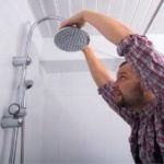 A man performing DIY shower plumbing work in a bathroom with tools, focused on home maintenance tasks.