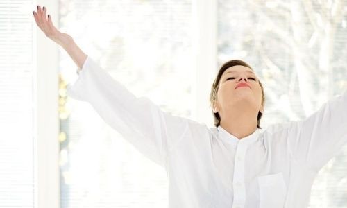 A woman in a white shirt smiles with arms raised in a bright space, reflecting positivity for B & D Plumbing, Heating & A/C.