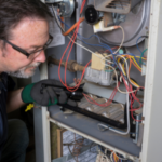 Male technician inspecting a heating unit's wires and components for B & D Plumbing, Heating & A/C services.