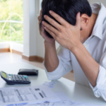 Distressed man with paperwork and calculator in bright indoor space, emphasizing the need for efficient heating services.