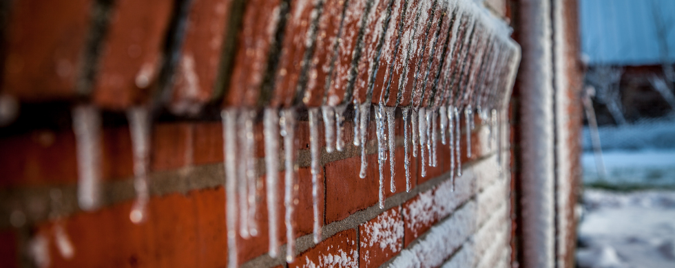 Close-up of a brick wall with icicles and frozen water, representing winter's impact on property maintenance.