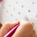 Hand with a pen marking the 27th on a calendar, highlighting HVAC service scheduling by B & D Plumbing.