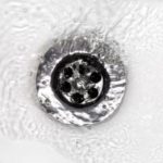 Metal drain cover with holes in swirling water, highlighting plumbing maintenance for B & D Plumbing, Heating & A/C.