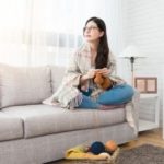 Woman knitting on a light couch with yarn and a lamp in a cozy indoor space by B & D Plumbing, Heating & A/C.