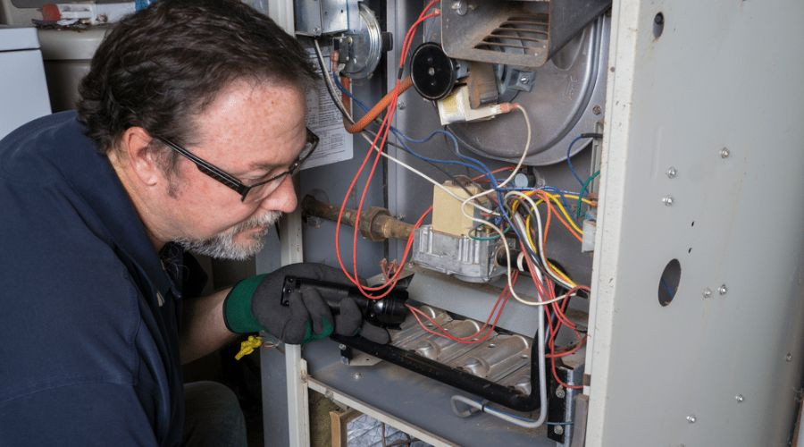 Technician repairing a furnace, showing components, wires, and tools for B & D Plumbing, Heating & A/C services.