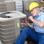 Male technician in a yellow hard hat servicing air conditioning unit on-site, emphasizing AC maintenance and repair services.
