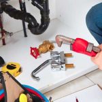 Person using a wrench on plumbing valves and pipes for maintenance at B & D Plumbing, Heating & A/C services.