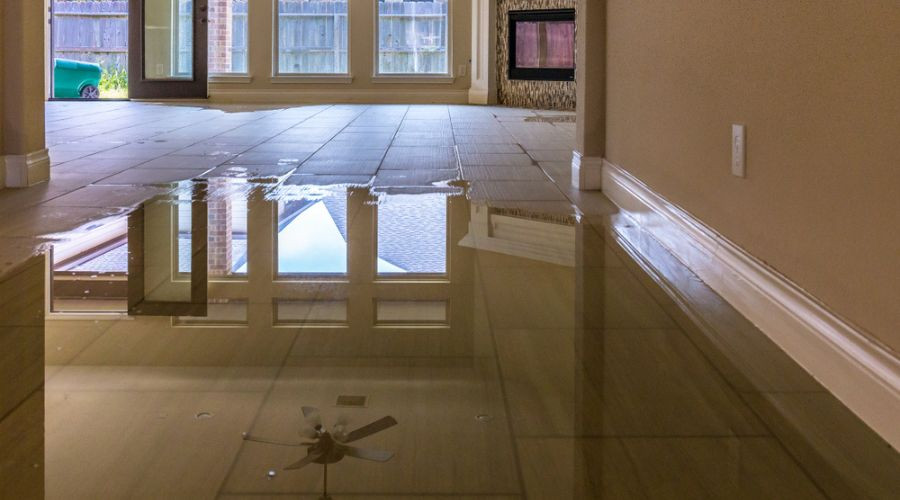 Interior of a home with water pooling on tiled floor, ceiling fan above, and fireplace visible, highlighting plumbing issues.