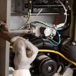 Technician performing maintenance on a heating system, using tools like a wrench in a mechanical environment.