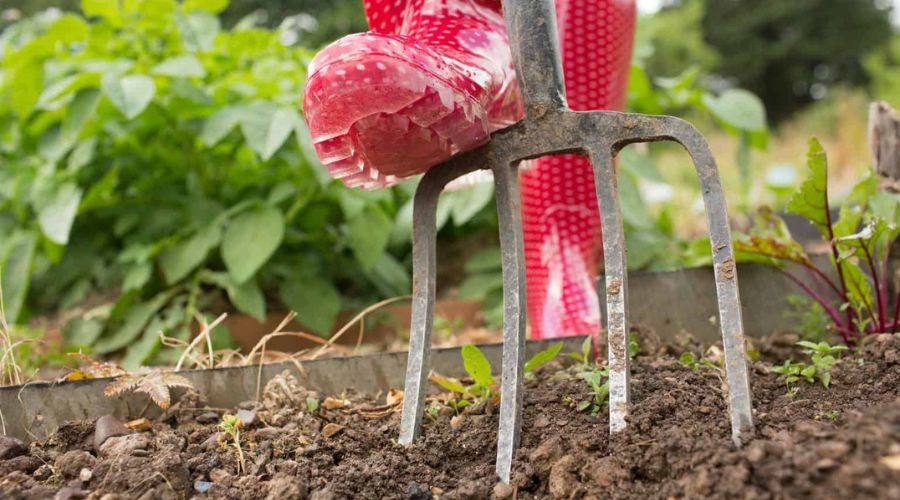 Garden fork in soil with red rubber gardening boots, reflecting B & D Plumbing's property maintenance theme.