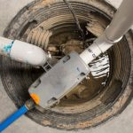 Sump pump and drainage pipes in a circular sump pit with water accumulation for basement flood prevention. B & D Plumbing.