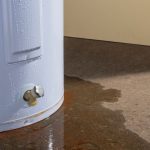 Traditional water heater tank with visible water leak on the floor, illustrating common issues related to water heater maintenance and repair.