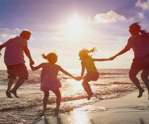 Family enjoying a beach day, jumping in the water during sunset, symbolizing summer fun and outdoor activities.