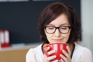 Woman with glasses enjoying a hot beverage in a cozy indoor setting, promoting comfort and relaxation during allergy season.