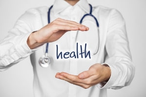 Person in a white shirt holding the word "health" with a stethoscope around their neck, emphasizing the importance of health in relation to seasonal allergy management and indoor air quality.