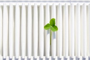 A green sprout emerging between white air conditioning fins, symbolizing the importance of regular maintenance and filter replacement for efficient A/C performance.